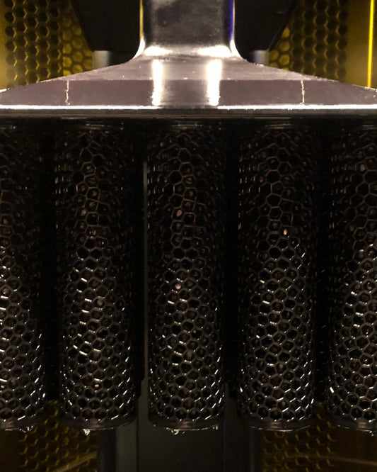 Puños Race Day recién impresos en malla 3D colgando de la plataforma de una impresora DLS de Carbon